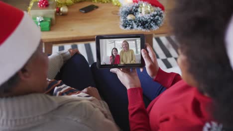 madre y hija afroamericanas usando una tableta para una videollamada de navidad con la familia en la pantalla