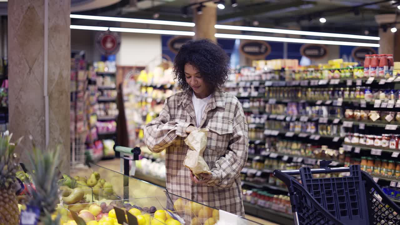 mujer elegante afroamericana eligiendo naranjas en el supermercado en una bolsa de papel
