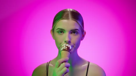 una mujer joven rubia atractiva comiendo un cono de helado con chocolate en un estudio con fondo infinito