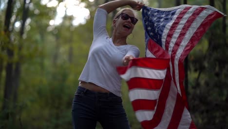 el primer plano de una linda mujer rubia bailando con una bandera americana y girándola a su alrededor