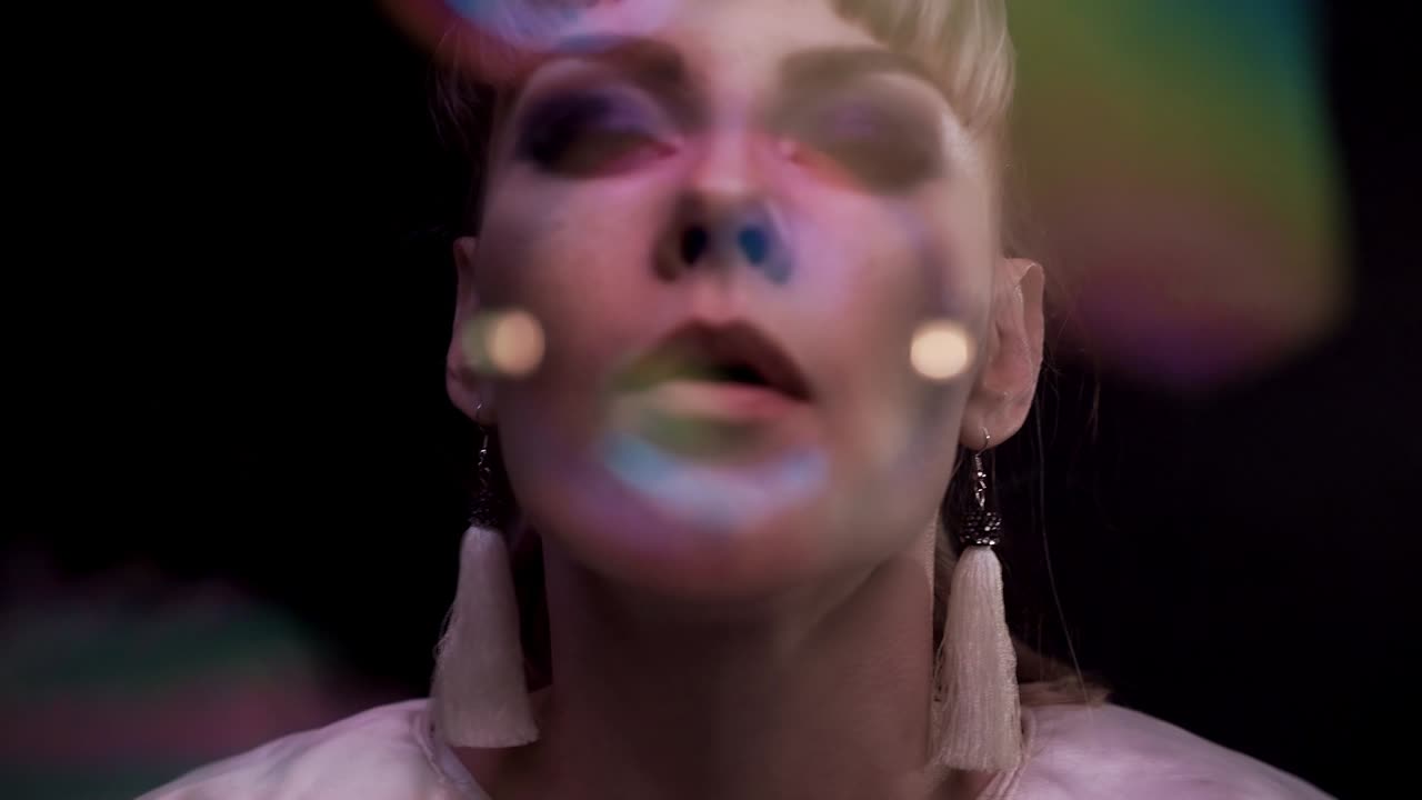 Closeup: Cute girl does tricks with soap bubbles. She blows a lot of small bubbles into the camera through soap screen.
