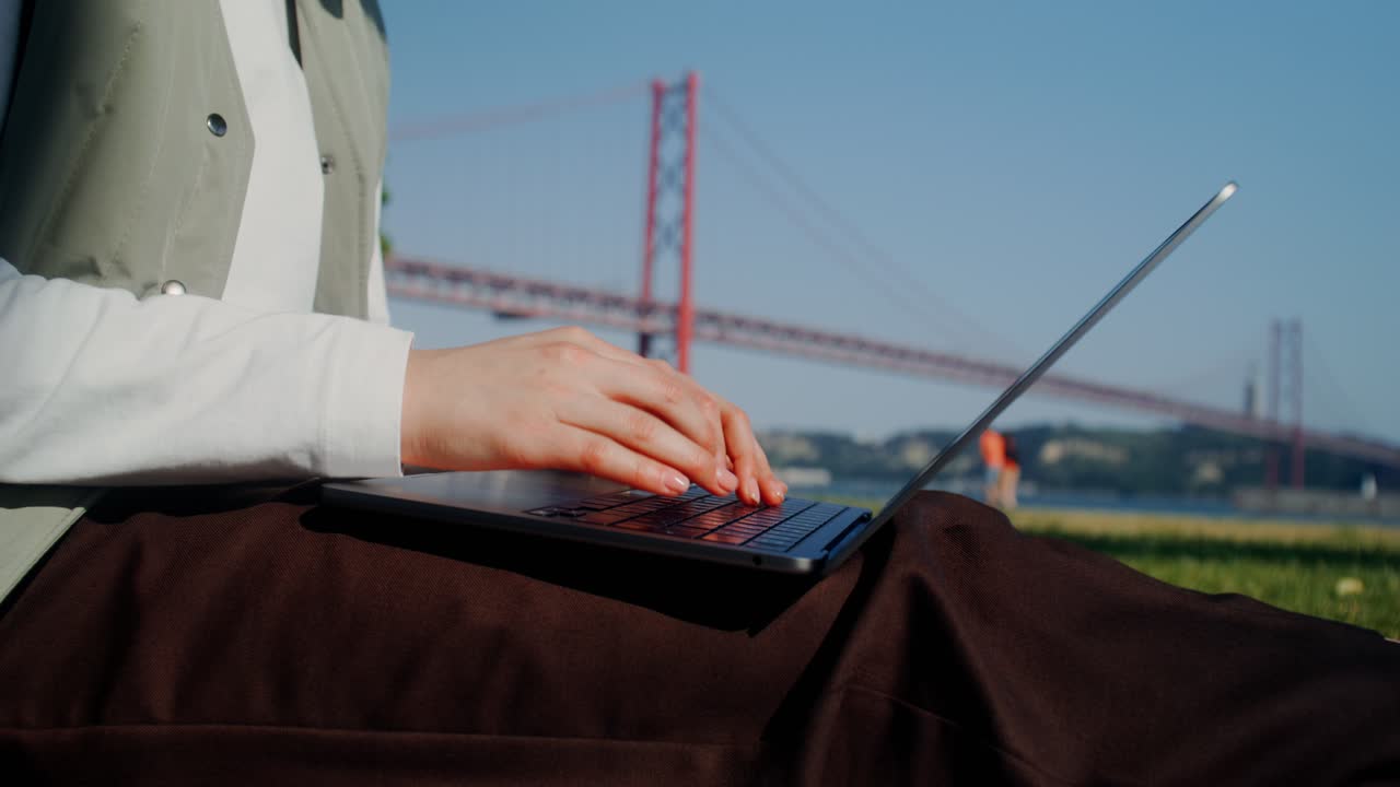 Vrouw werkend op een laptop in een park bij een brug