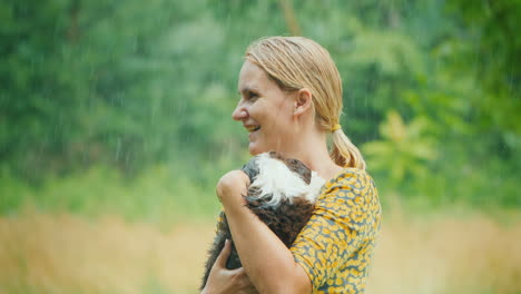 mujer mojada con un vestido de verano con un cachorro en los brazos bajo la lluvia cálida