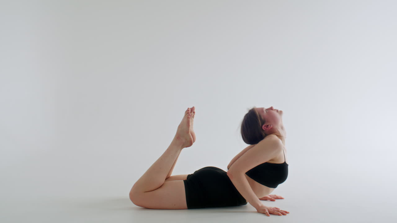 Mädchen macht Yoga-Rückbeuge, bei der die Füße den Kopf in einem minimalistischen Studio berühren