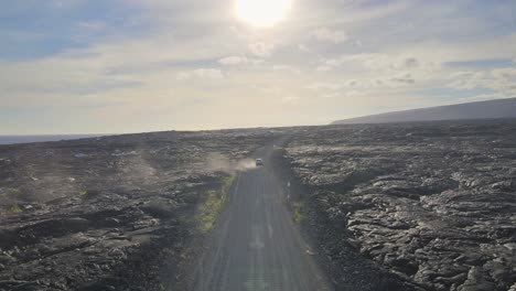 impresionante vista aérea de un coche conduciendo hacia la puesta de sol ardiente por encima de un campo de lava volcánica en big island, hawai