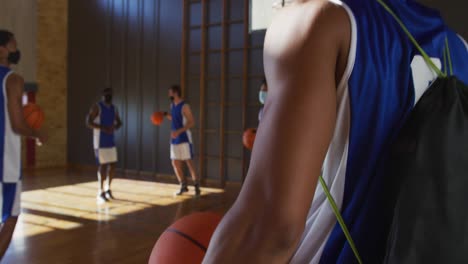 equipo de baloncesto masculino diverso usando máscaras faciales y saludando con codos