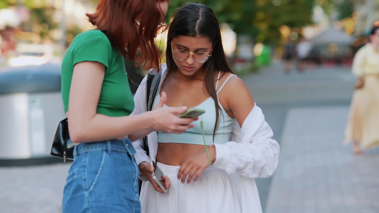 dos mujeres jóvenes usando un teléfono inteligente en la calle