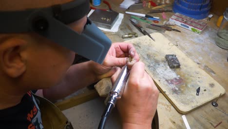 male jewelry maker using a motor polish tool on a piece of jewelry in a jewelry making workshop