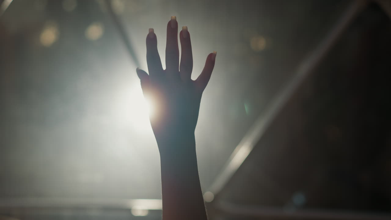 la mano de la mujer se abre y cierra en un primer plano en una habitación oscura. la silueta de la mano de la dama hace gestos graciosos a la luz de fondo brillante en un estudio oscuro. señales de lenguaje corporal