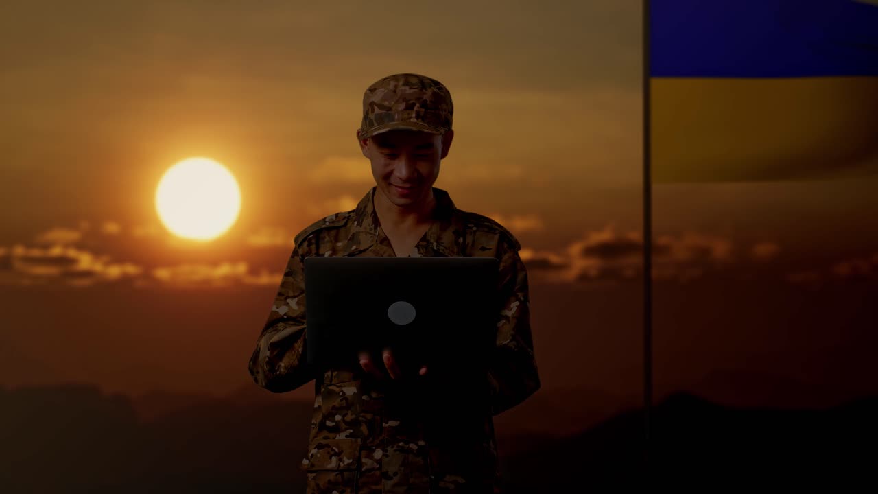 Soldier using a laptop during sunset with Ukrainian flag in background