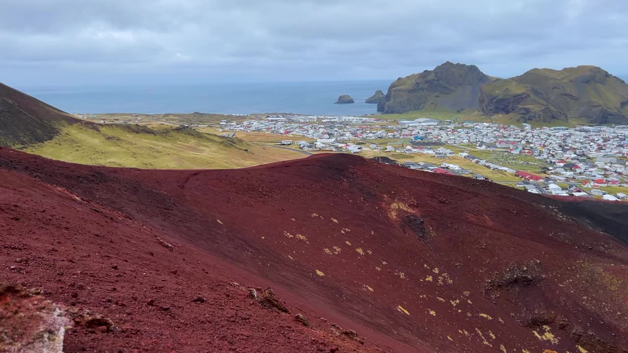 Red Rock Foreground Of Eldfell Volcano Overlooking Vestmannaeyjar Hamlet (Westman Islands) In Iceland. Aerial Wide Shot