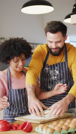 vertical video of happy diverse couple baking in kitchen, kneading dough