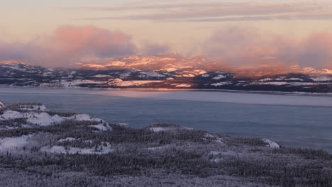 snow-covered forest and mountain with frozen lake laberge during winter in yukon, canada. - aerial shot