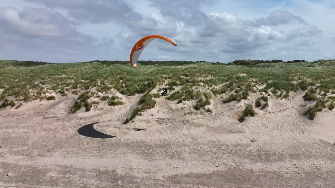 toma aérea de un parapente montando la banda de elevación de una duna cubierta de hierba verde con arena blanca en un día soleado junto al mar en ouddorp, brouwersdam, países bajos