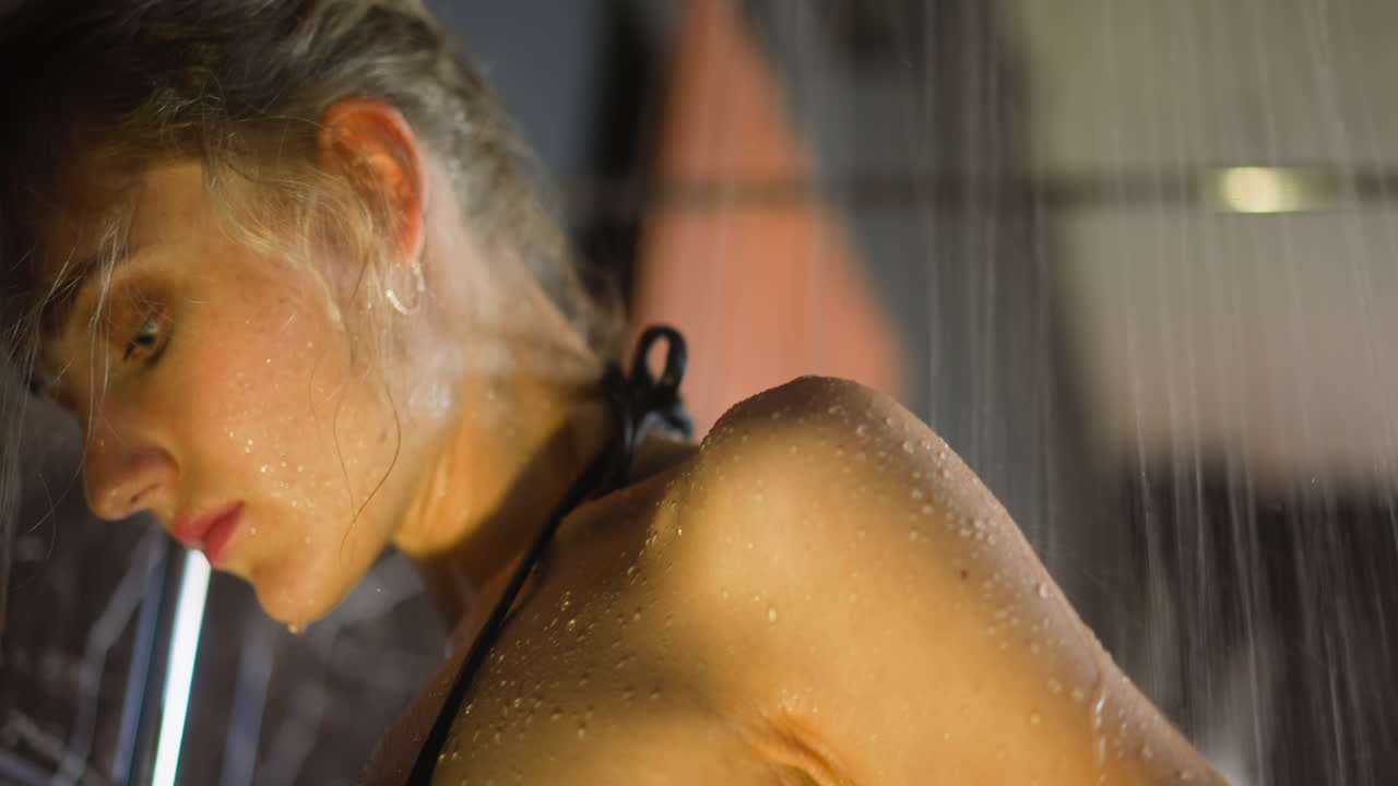 mujer rubia pone de nuevo bajo los chorros de agua que caen en la ducha