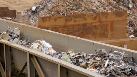 conveyor belt at a recycling plant carrying sorted waste against a backdrop of a large pile of mixed debris