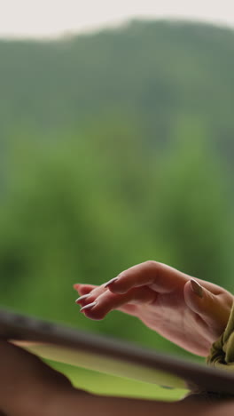 woman in green t-shirt holds laptop computer and adjusts hair lock against distant mountains at eco resort close side view slow motion