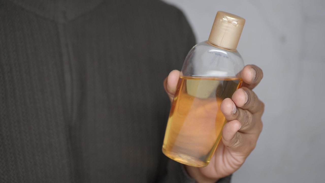 Primer plano de una mano sosteniendo una botella transparente de aceite cosmético amarillo