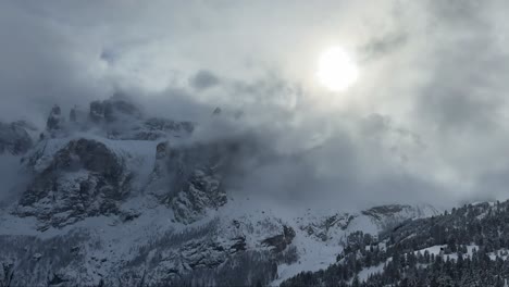 snow-covered mountain peaks under a cloudy sky with the sun partially visible