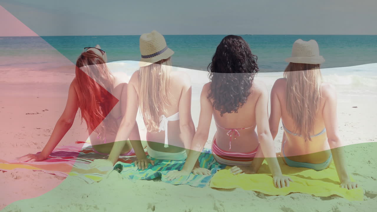 Sitting on beach towels, four women facing ocean with flag animation overlay