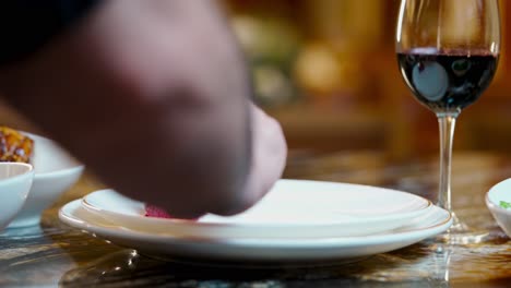 close-up of a chef decorating a plate with beetroot sauce on a served table with a glass of wine