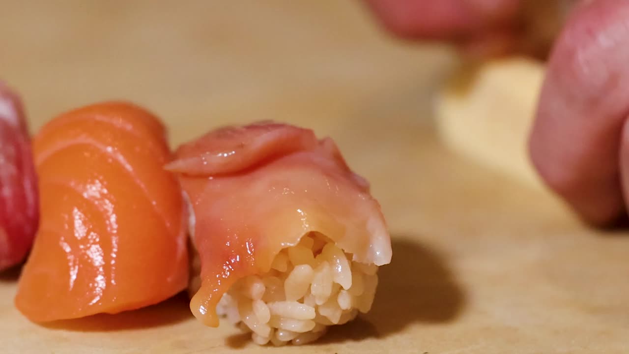 Extreme close-up of a chef's hands meticulously assembling tamago and fresh nigiri sushi pieces