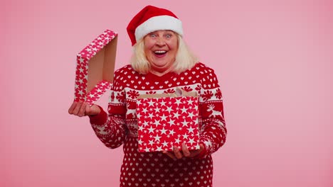 grandmother in christmas sweater smiling unwrapping gift opening box with pet cat great surprise