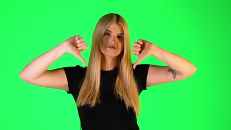 pretty blonde woman thumbs down gesture, studio portrait with green background