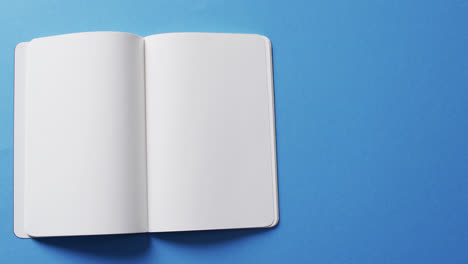 Close-up-of-open-blank-book-with-copy-space-on-blue-background-in-slow-motion