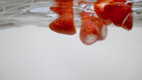 red strawberries adding natural flavor to fresh water, underwater shot