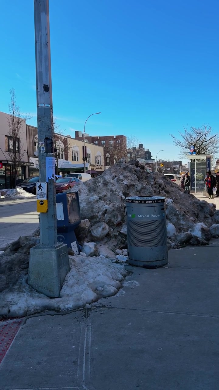 New York, USA, 25 gennaio 2026: Grande cumulo di neve sporca sul marciapiede accanto al bidone della raccolta differenziata. Enorme cumulo di neve grigia su un marciapiede cittadino accanto a un bidone argentato per la raccolta differenziata della carta mista e un'edicola.