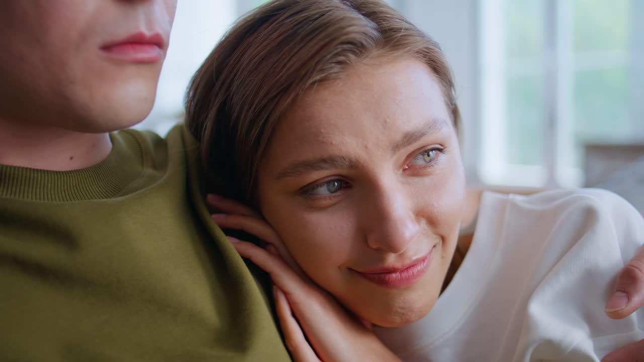 Cute girl leaning boyfriend shoulder watching movie sofa closeup. Pair embracing