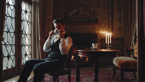man drinking a cup by a fireplace
