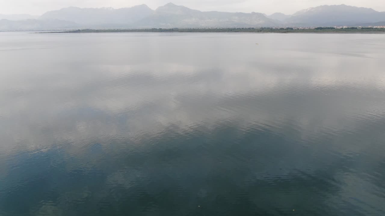 Drone view in Albania flying over Shkod&euml;r green color lake in Pogradec top view on cloudy day and mountains in the horizon