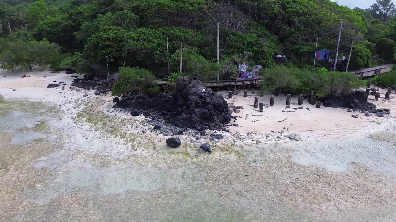 Semi orbit around dark rocks and tropical trees on a remote beach in Gili Trawangan