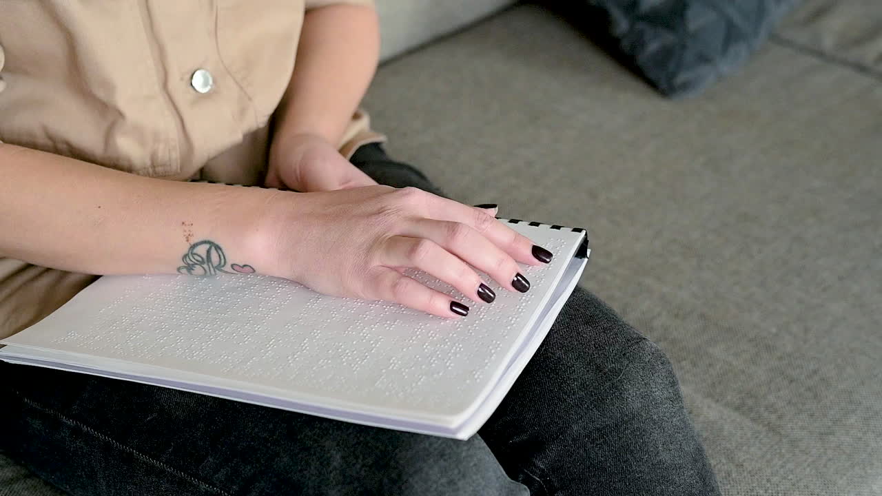 la cámara se enfoca en la mano de una mujer leyendo un libro en braille sentado en el sofá de casa