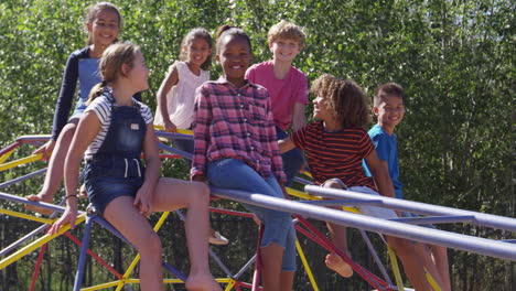 Pre-teen-friends-sitting-on-climbing-frame-in-playground