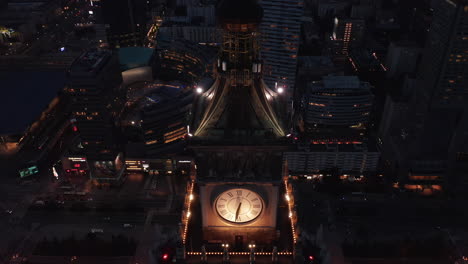 Descending-fly-around-large-illuminated-tower-clock.-Evening-aerial-footage-of-downtown-cityscape.-Warsaw,-Poland