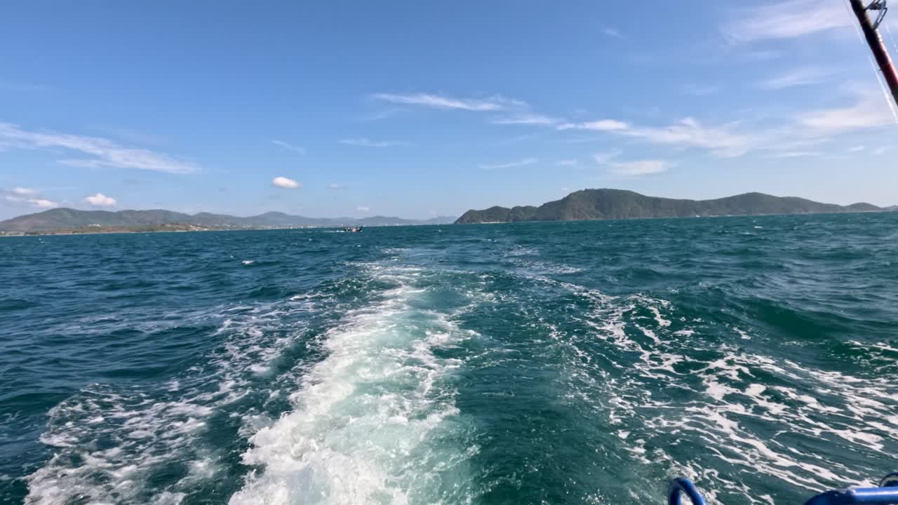 A longtail boat speeds through clear blue waters near Phuket, Thailand, under a bright sky, creating a dynamic wake