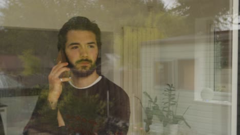 el ritmo masculino mientras usa un teléfono inteligente y se detiene para mirar por la ventana