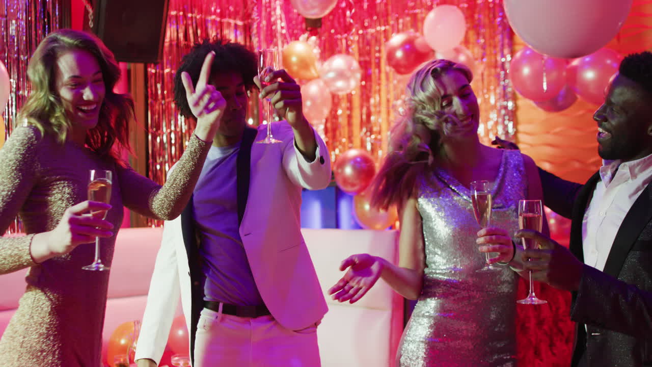 Video of a diverse group of happy friends dancing with glasses of champagne at a nightclub
