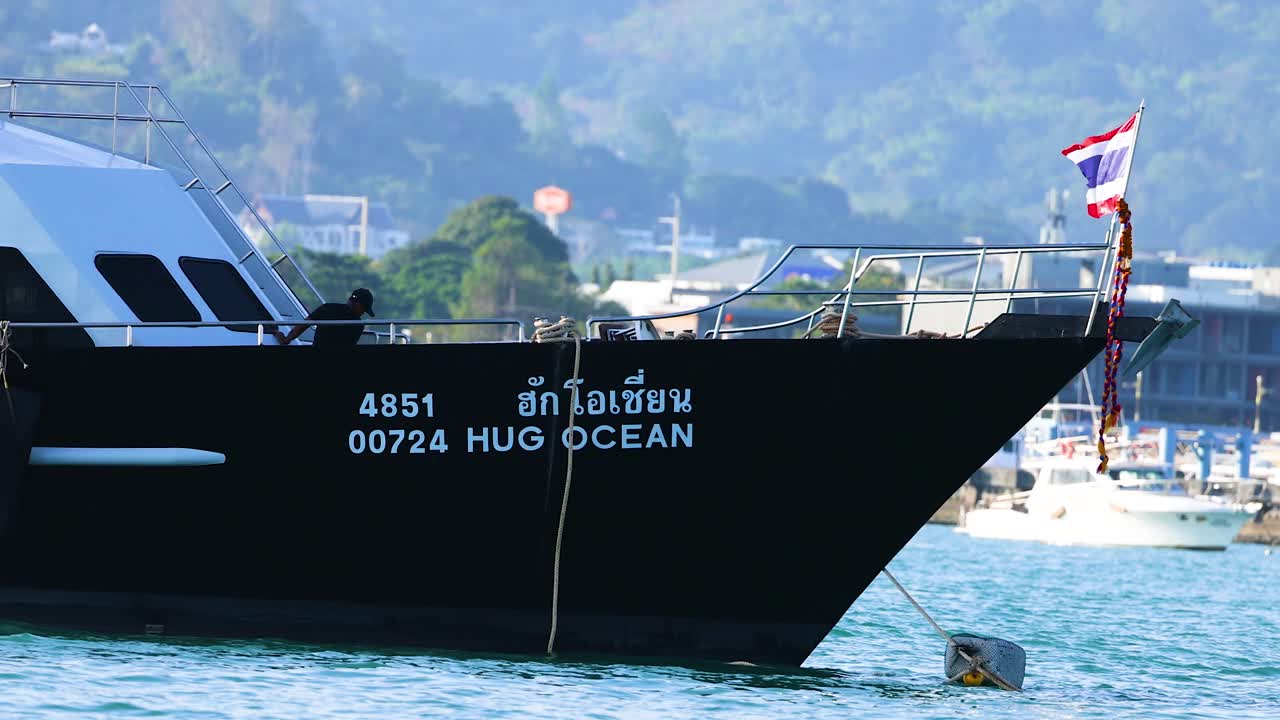 A fishing boat with a Thai flag moves through Phuket harbor under clear skies, showcasing vibrant colors and serene waters
