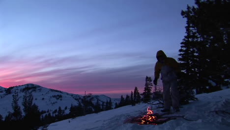 panning shot from snowy mountains to a hiker tending a campfire