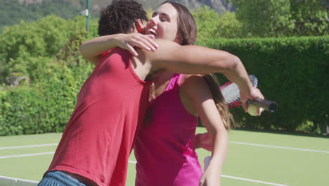 feliz pareja biracial con raquetas de tenis abrazándose en el jardín en un día soleado
