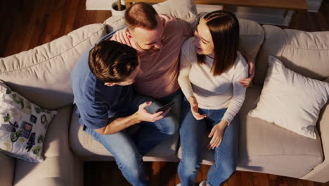 three people sitting on a couch, looking at a phone together