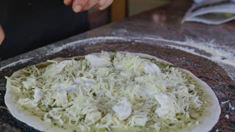 persona rociando queso mozzarella en una pizza casera