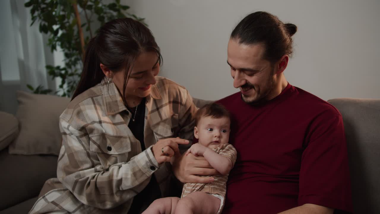 Close up of happy parents a young girl and a man in a red t-shirt holding their little baby daughter in their arms and playing with her during their Happy time at home together as a family in a modern apartment