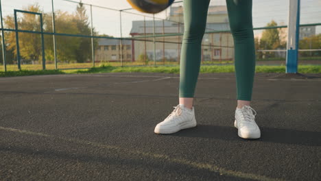 close-up leg view of athletic woman bouncing volleyball outdoors on court, basketball hoop and a building are visible in the background, showcasing active recreation in a vibrant urban setting