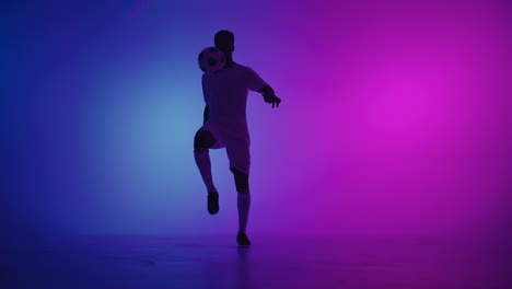 black man a player juggles football ball in a dark studio with neon lights on the floor and red and blue lighting effects in slow motion. african professional football soccer player