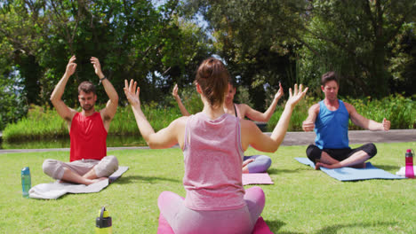 rear view of caucasian female instructor practicing yoga with diverse group in park